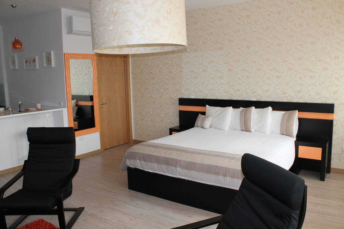 Une chambre à coucher avec un lit, deux chaises, un miroir et une armoire en bois.