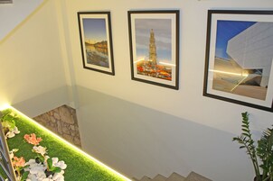 A staircase with a green artificial grass border, framed pictures of a cityscape and a building, and a potted plant.
