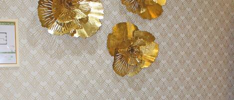 A teal chair with a metal frame, a patterned wallpaper, and three gold decorative pieces on the wall.