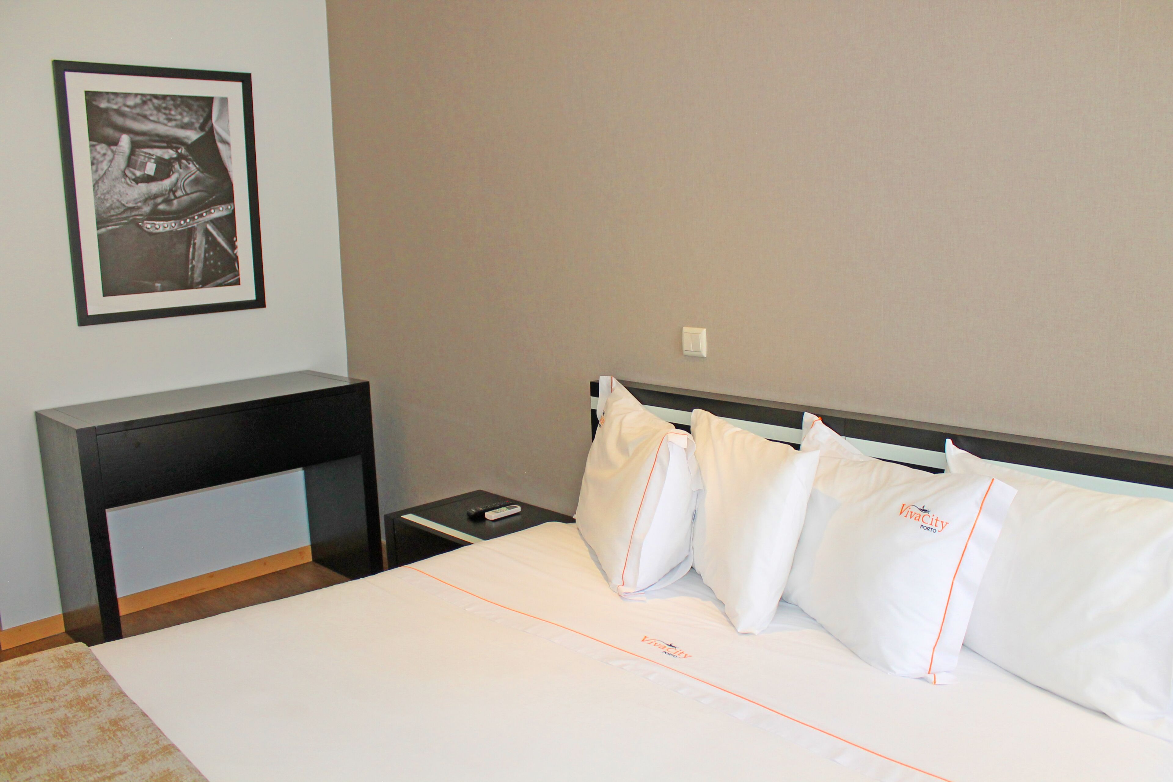 Une chambre d’hôtel avec un lit, des oreillers blancs, une table de chevet, une télécommande et un tableau encadré au mur.