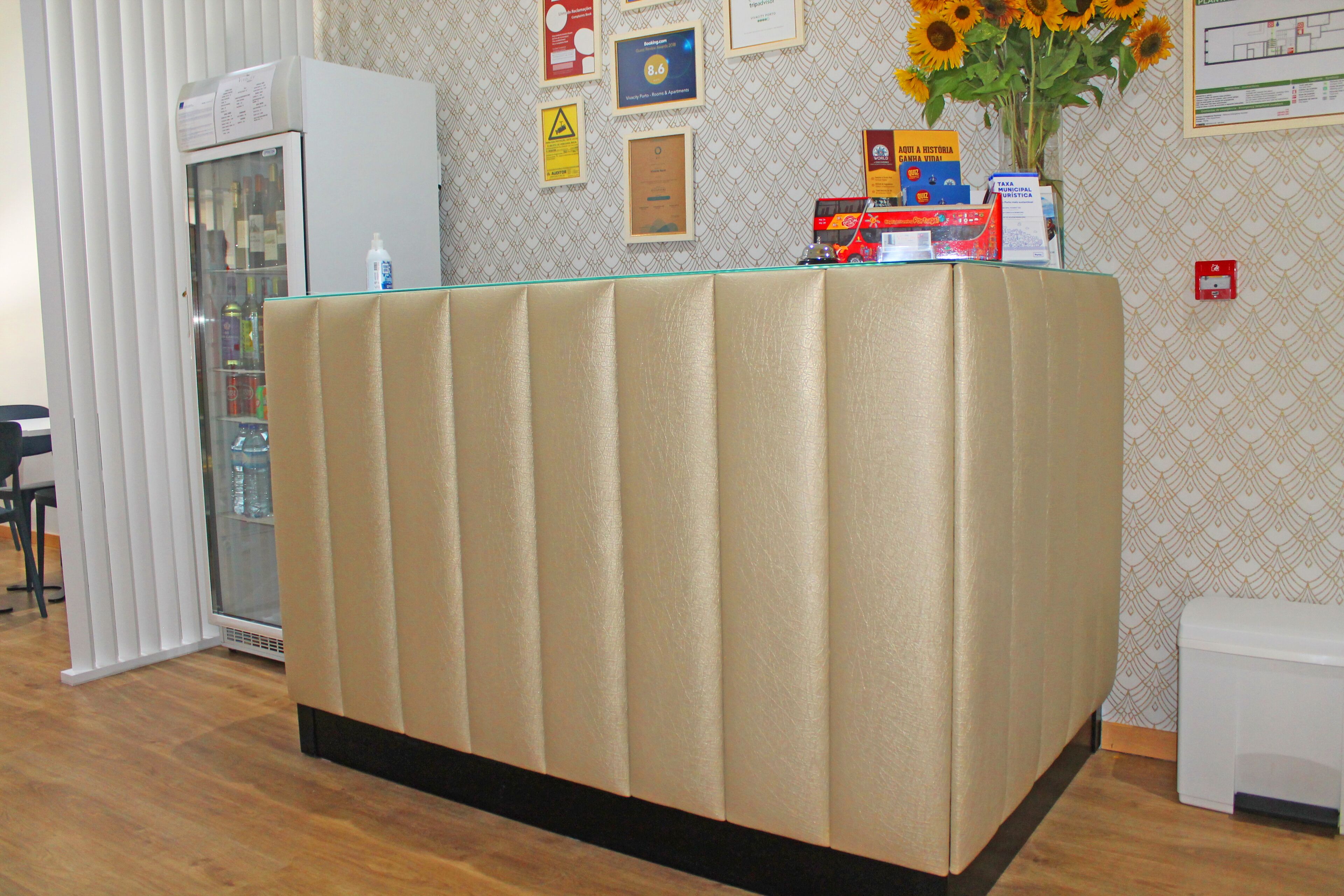 A reception desk with a glass top, a white refrigerator, and a wall decorated with certificates and a vase of sunflowers.
