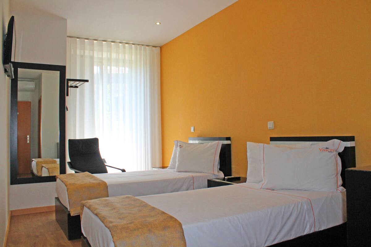 Une chambre d’hôtel avec deux lits, une chaise, un miroir et une fenêtre avec des rideaux.