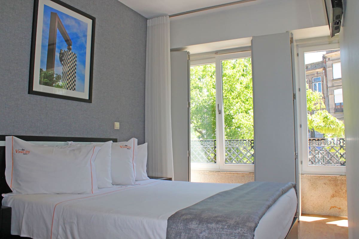 Une chambre d’hôtel avec un lit, un tableau encadré au mur et un balcon donnant sur un paysage verdoyant.