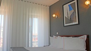 A hotel room with a large bed, white bedding, a framed picture on the wall, and a window with sheer curtains. - VivaCity Porto (Porto)