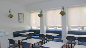 Un comedor con mesas, sillas, una barra y plantas colgantes.