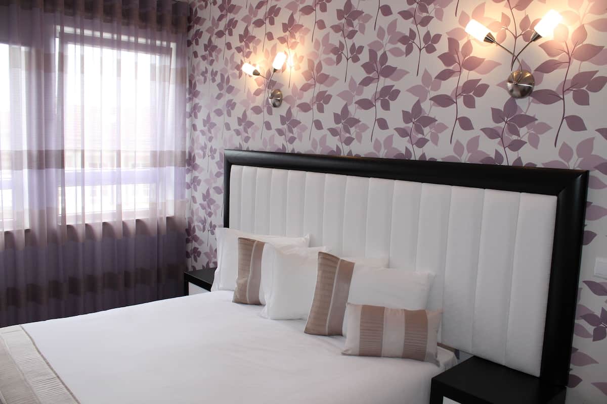 Une chambre d’hôtel avec un grand lit, une tête de lit et des lampes fixées au mur.