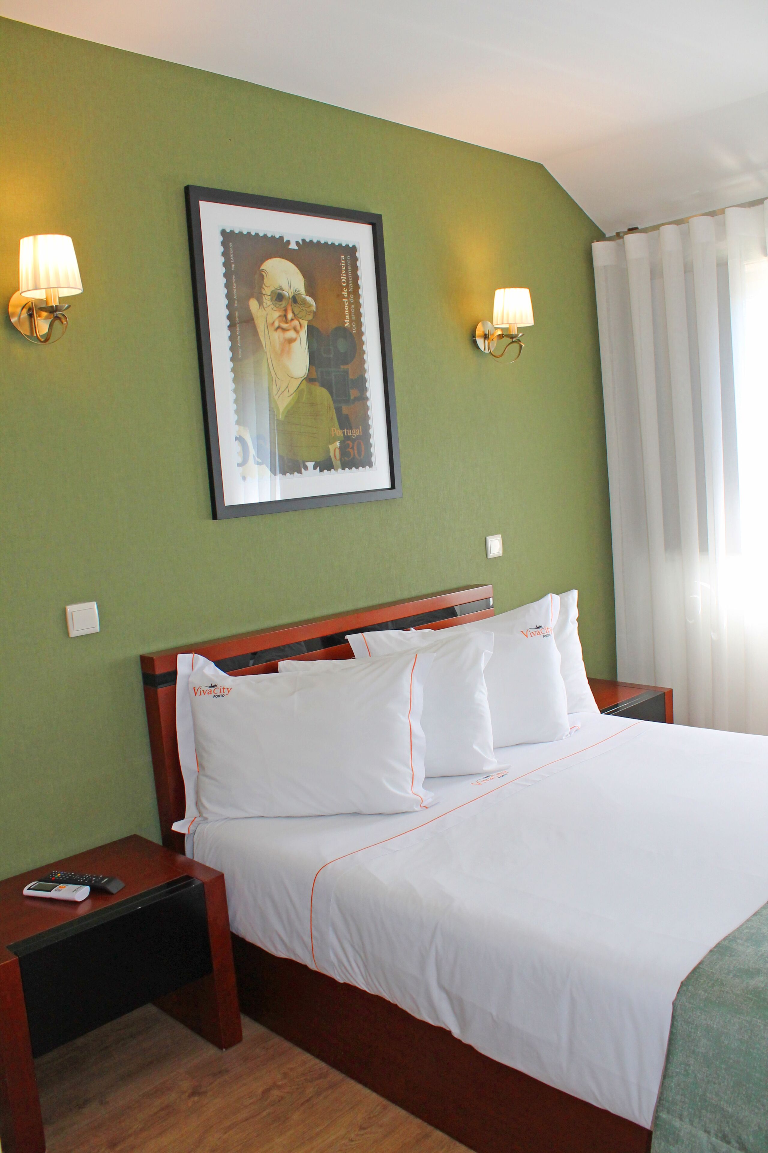 A hotel room with a large bed, two bedside tables, a framed picture on the wall, and a window with curtains.