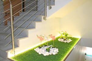 A staircase with a metal railing and a planter with white pebbles and pink and white flowers on a green artificial grass surface.