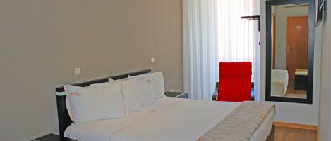 A hotel room with a large bed, a nightstand, a red chair, and a mirror on the wall.
