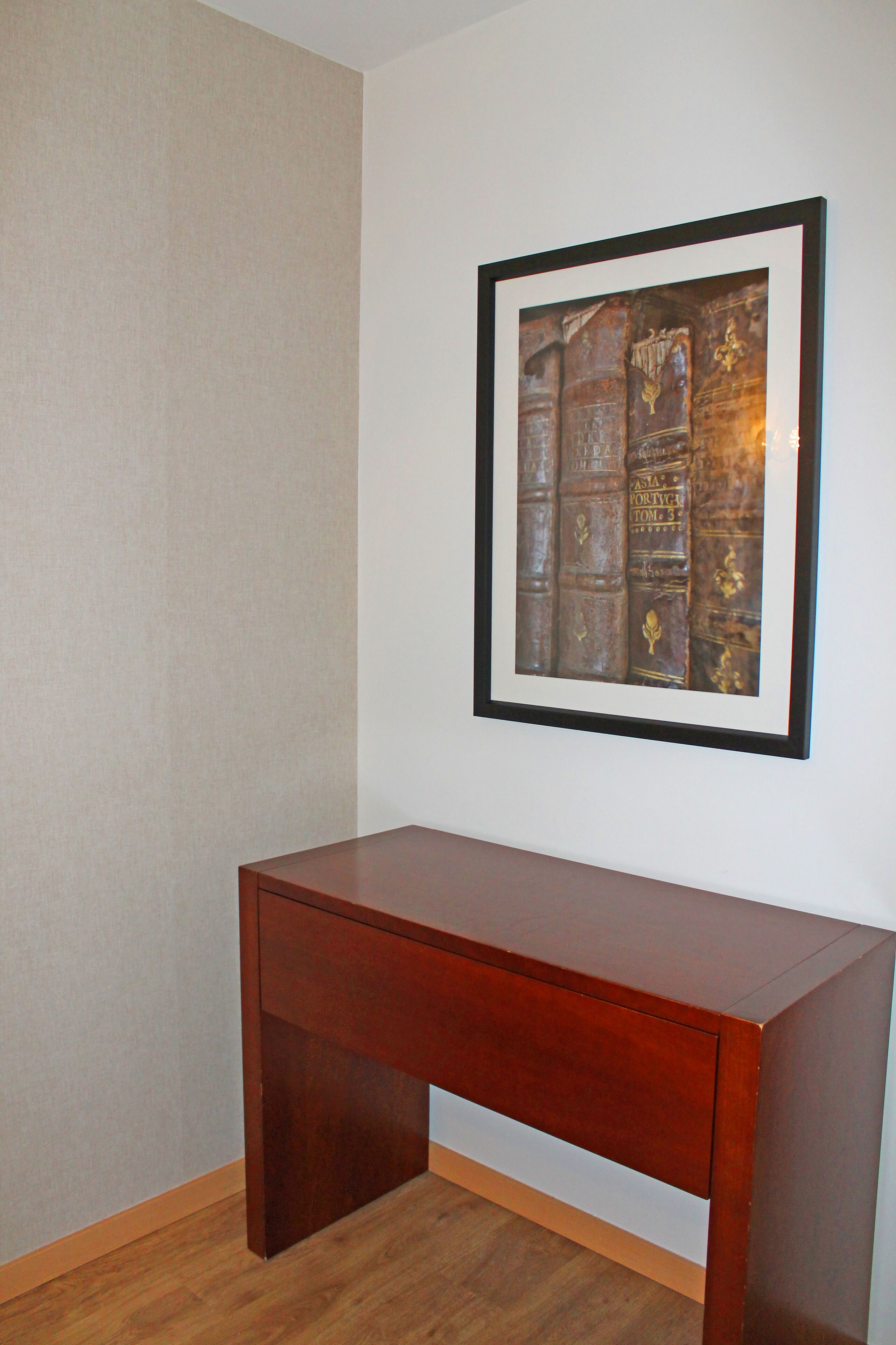 A wooden desk against a wall with a framed picture of books.