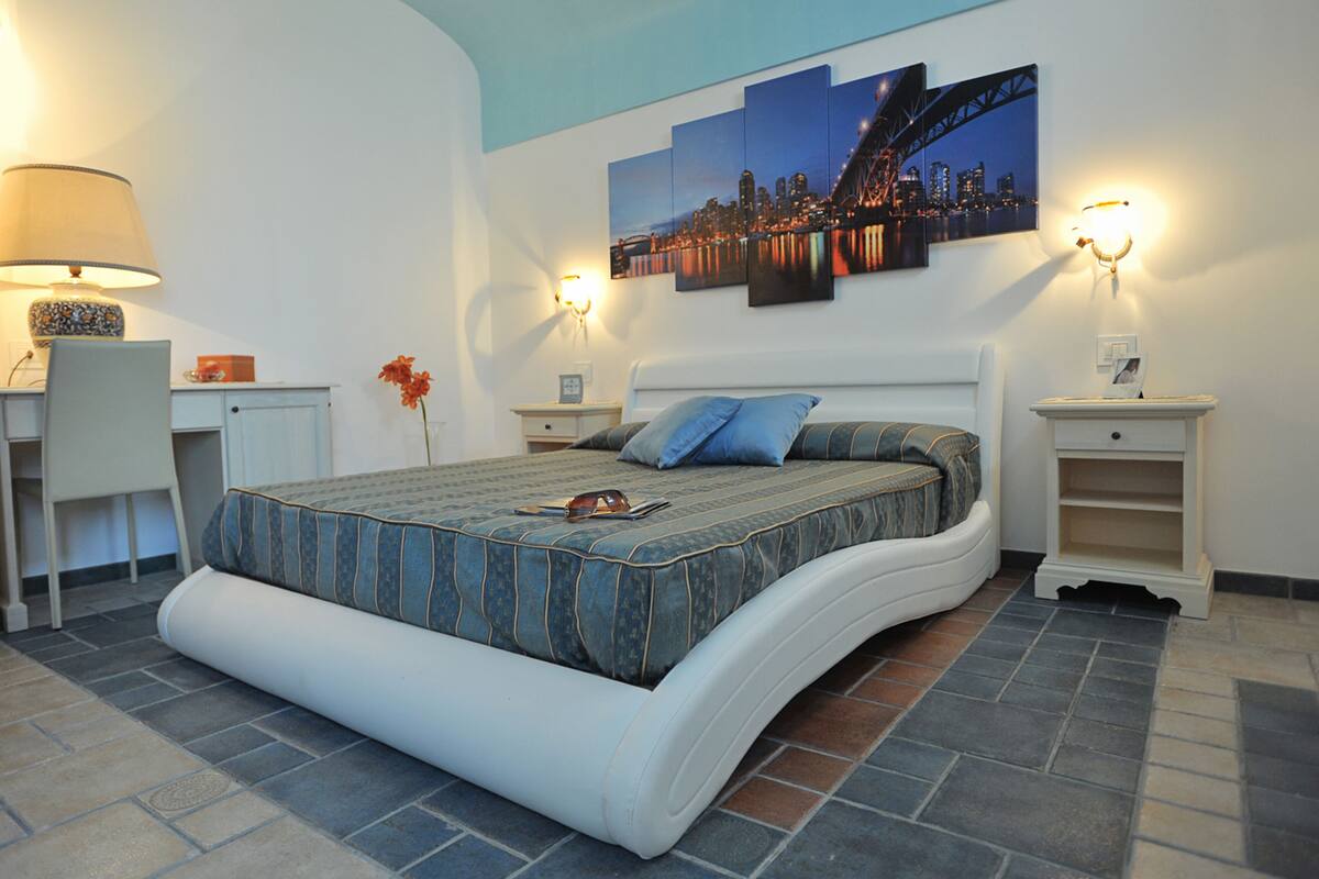 Un dormitorio con cama, mesitas de noche, un escritorio y un cuadro de un paisaje urbano en la pared.