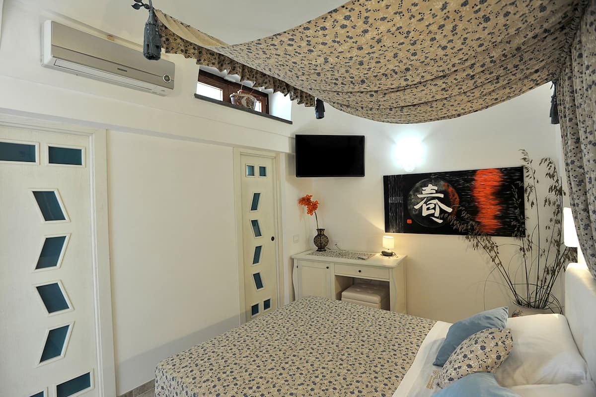 Un dormitorio con cama, escritorio, televisor y ventana con cortinas.