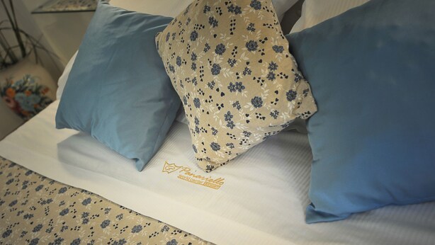 A bed with a floral-patterned pillow, a blue pillow, and a white pillow.