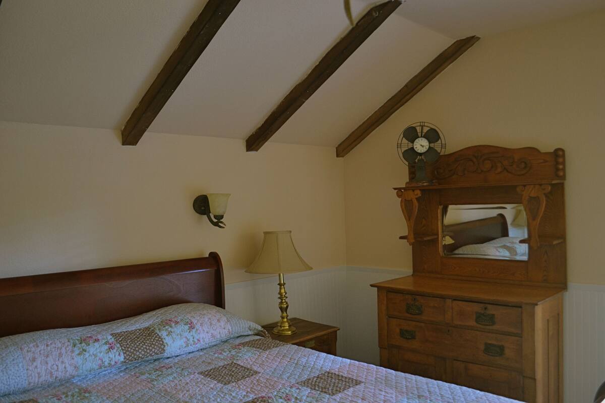Une chambre à coucher avec un lit en bois, une table de chevet avec une lampe, une commode et une horloge murale.