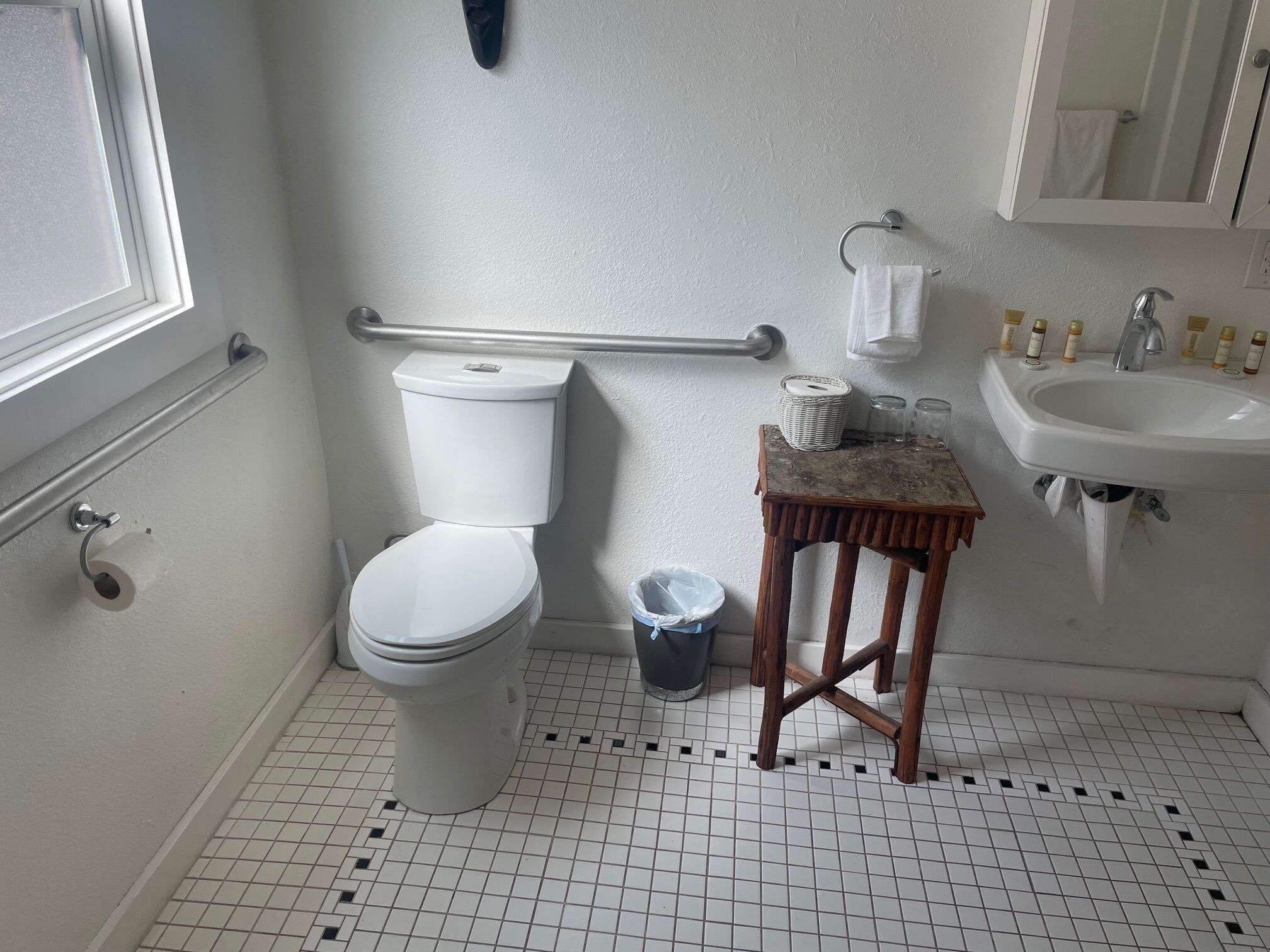 A bathroom with a toilet, a small wooden stool, a sink, and a mirror.