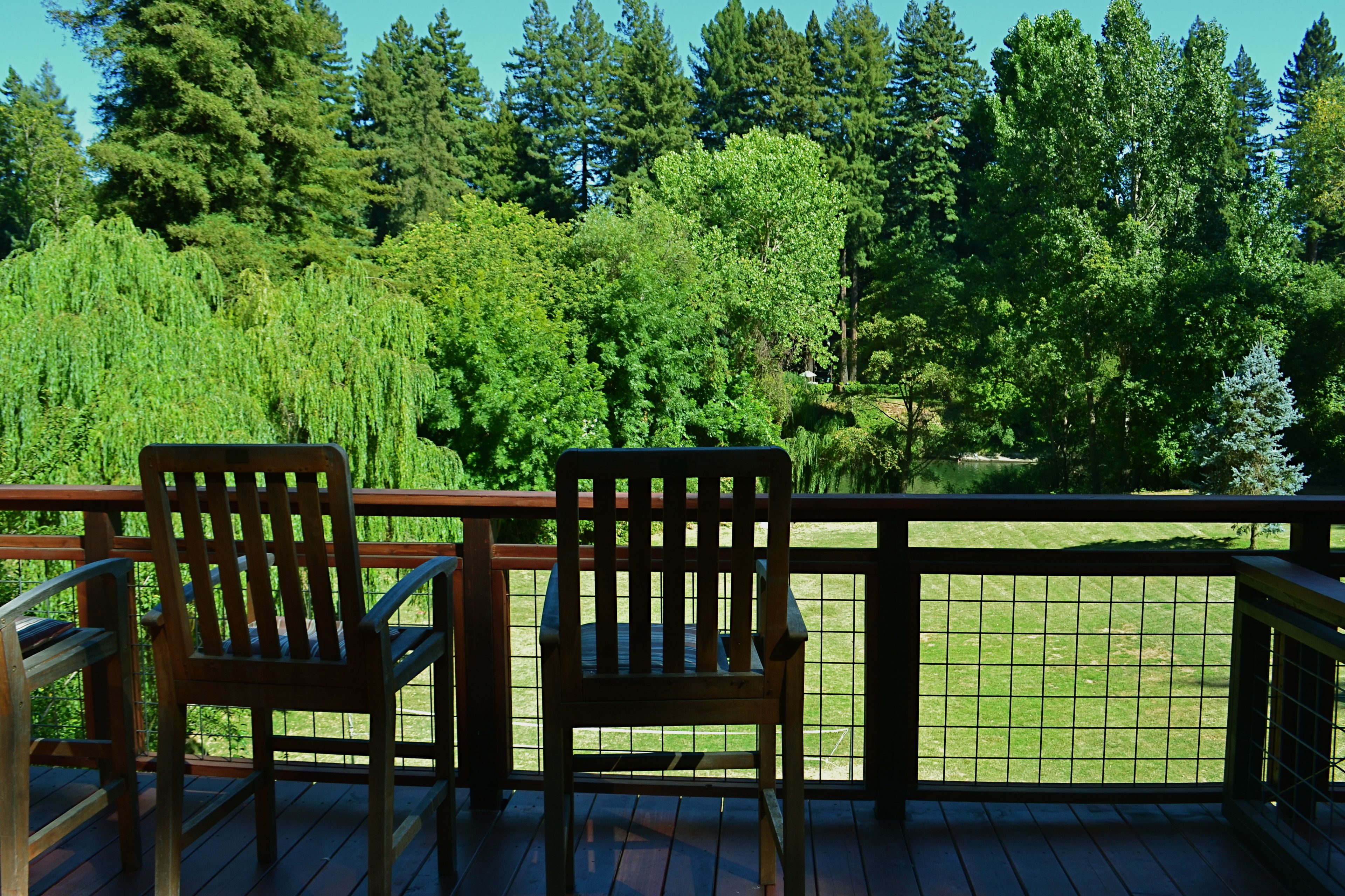 A deck with two wooden chairs and a view of a well-maintained lawn and trees.