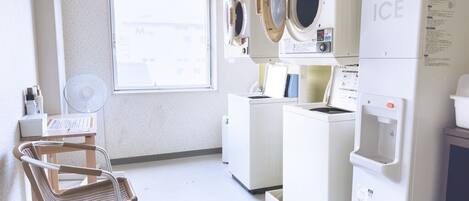 A laundry room with a washing machine, dryer, and a water dispenser. There is a chair and a window in the room.
