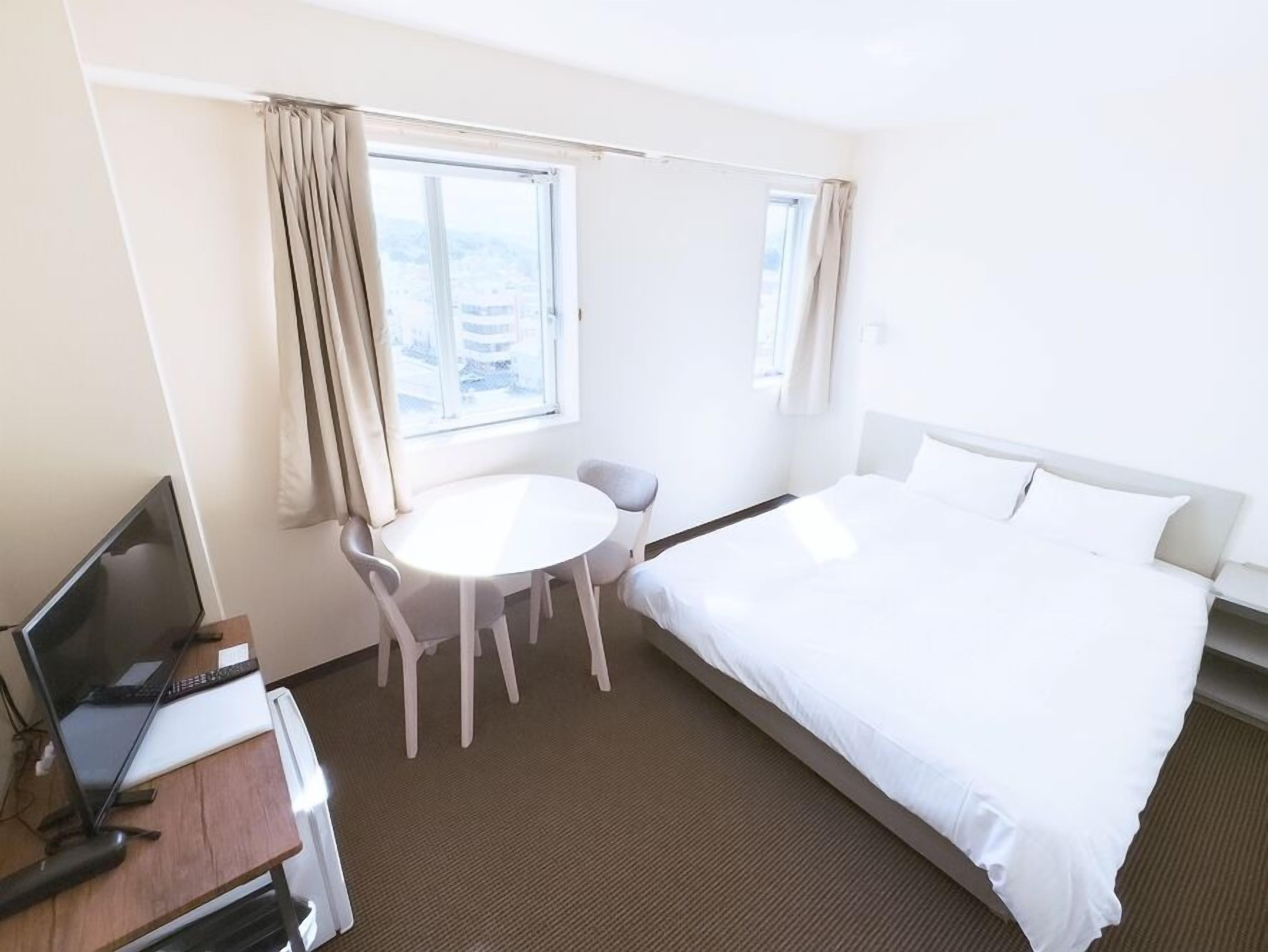 Una habitación de hotel con una cama, un escritorio con una computadora, una silla y una ventana.