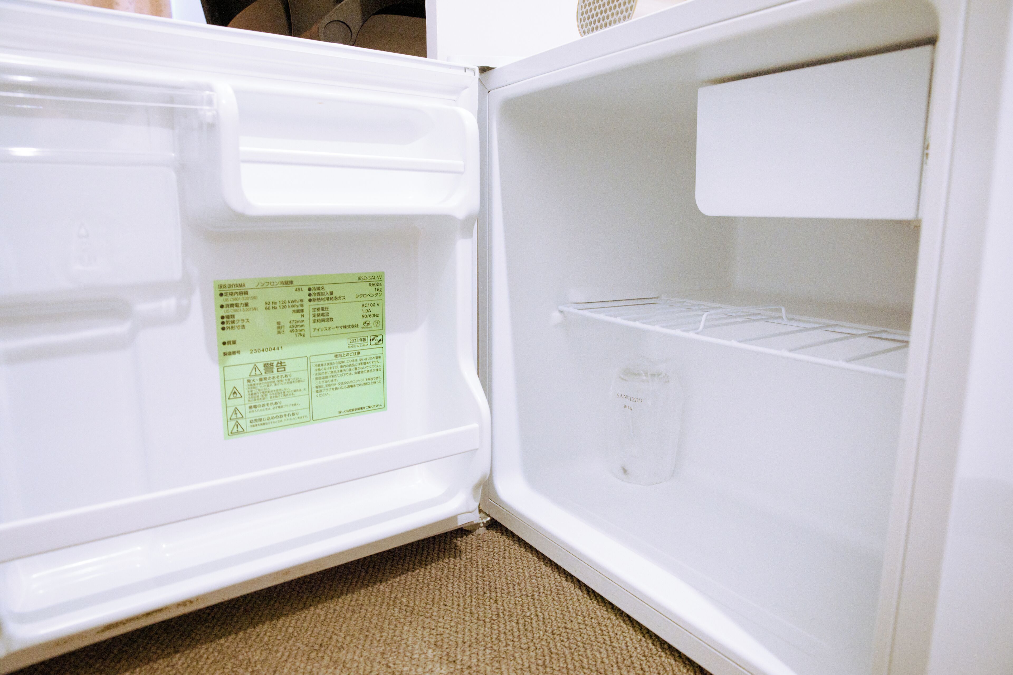 An open refrigerator with a green sticker on the door, a water dispenser, and a shelf.