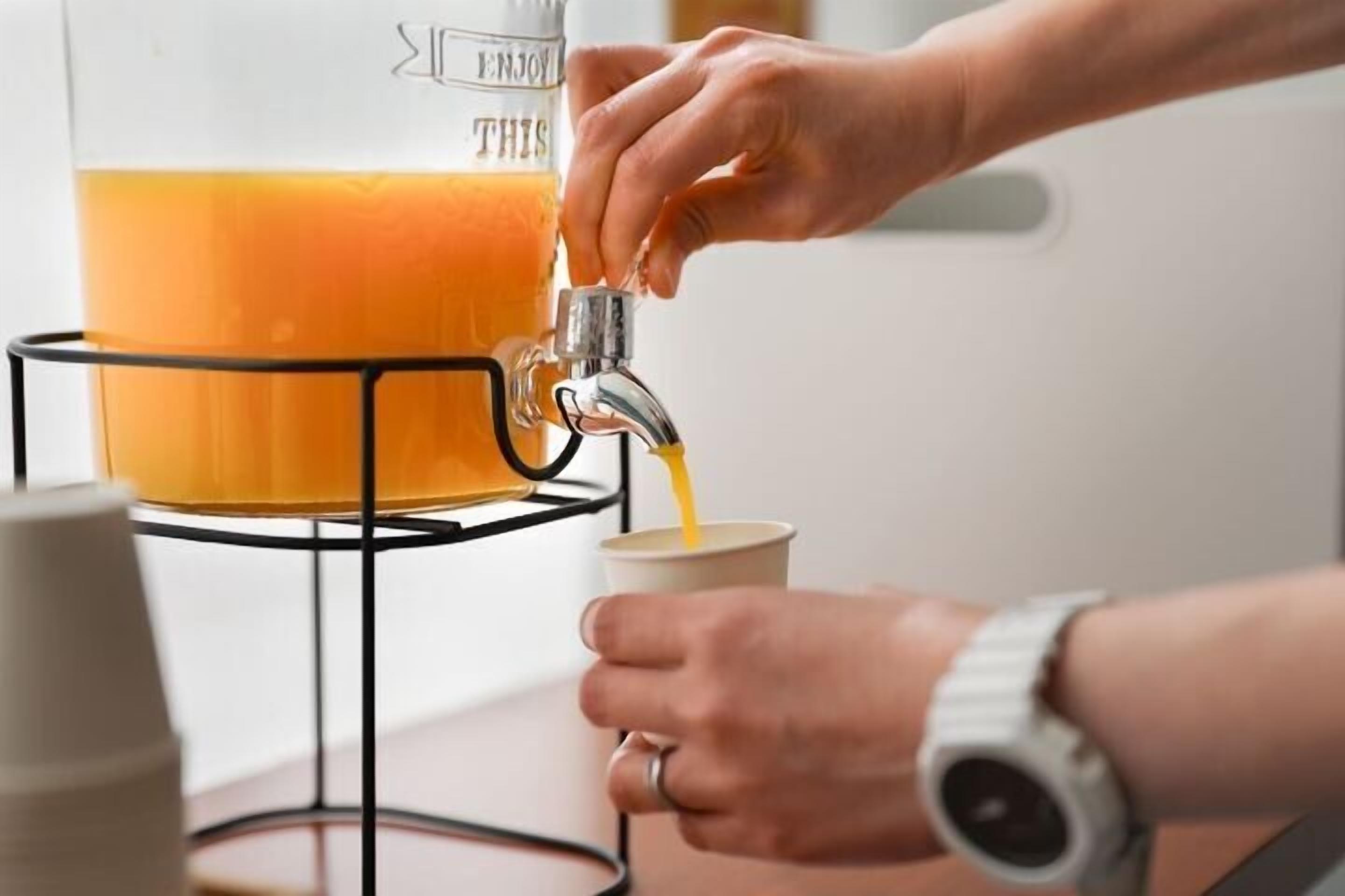 Una persona vertiendo líquido anaranjado desde un recipiente grande a una taza.