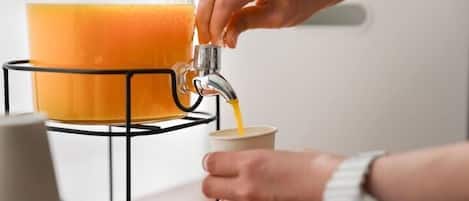 Una persona vertiendo líquido anaranjado desde un recipiente grande a una taza.