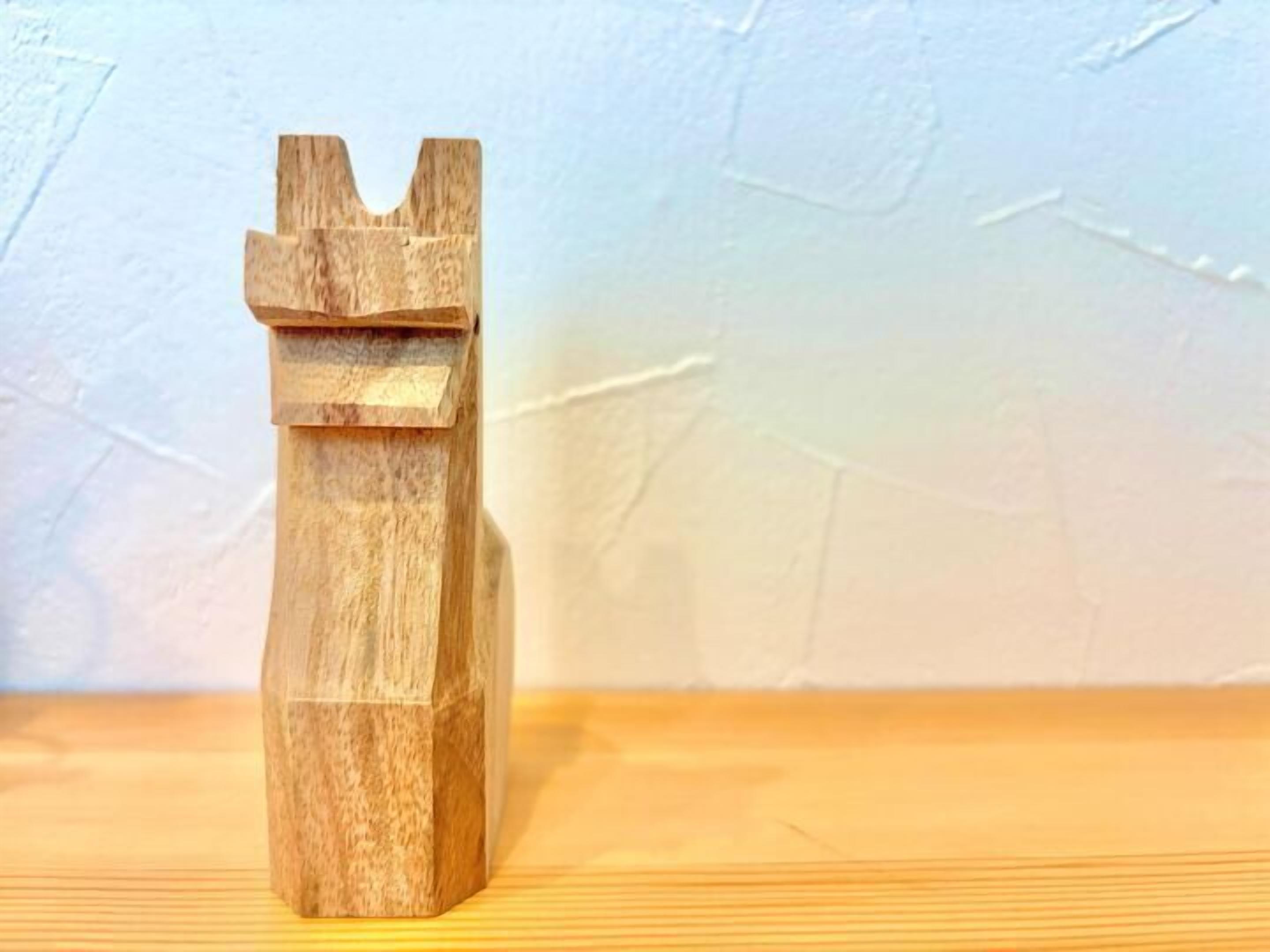 A wooden sculpture with a simple, geometric design, placed on a wooden surface against a plain wall.