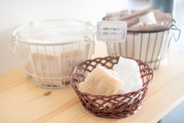 Una estantería de madera con tres recipientes: un contenedor de plástico transparente con tapa, una cesta de mimbre con una toalla blanca y otra cesta de mimbre con una toalla marrón.