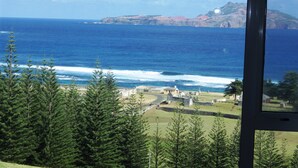 A coastal view with a clear sky, ocean waves, and a distant rocky island. - Panorama Seaside Apartments (Norfolk Island)