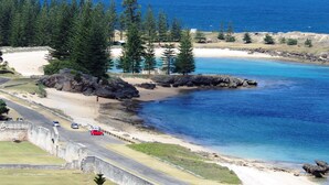 A coastal road with a beach and ocean view, surrounded by trees and a stone wall. - Panorama Seaside Apartments (Norfolk Island)