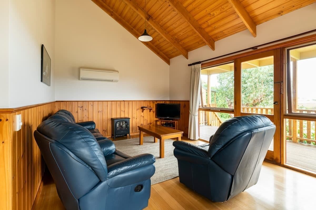 Een gezellige woonkamer met twee leren fauteuils, een houten salontafel, een televisie en een groot raam met uitzicht op groen.