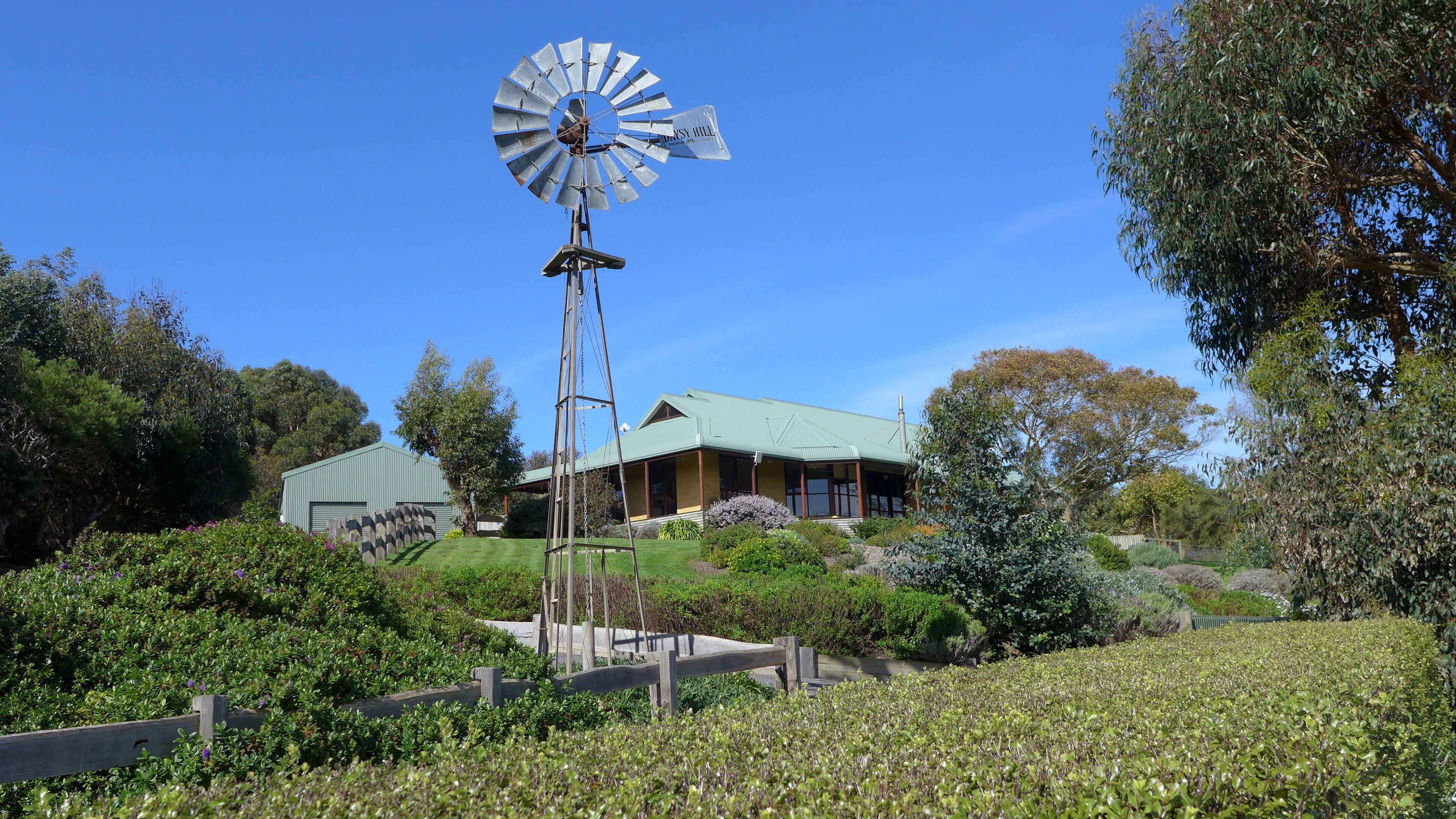 A windmill, a house with a green roof, and surrounding greenery.