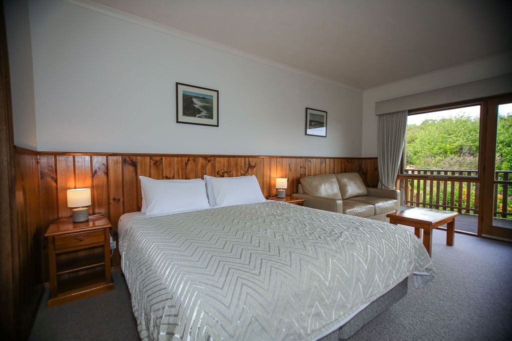 Ein Hotelzimmer mit einem großen Bett, einem Sofa, einem kleinen Tisch und einem Balkon mit Blick auf Grünflächen.
