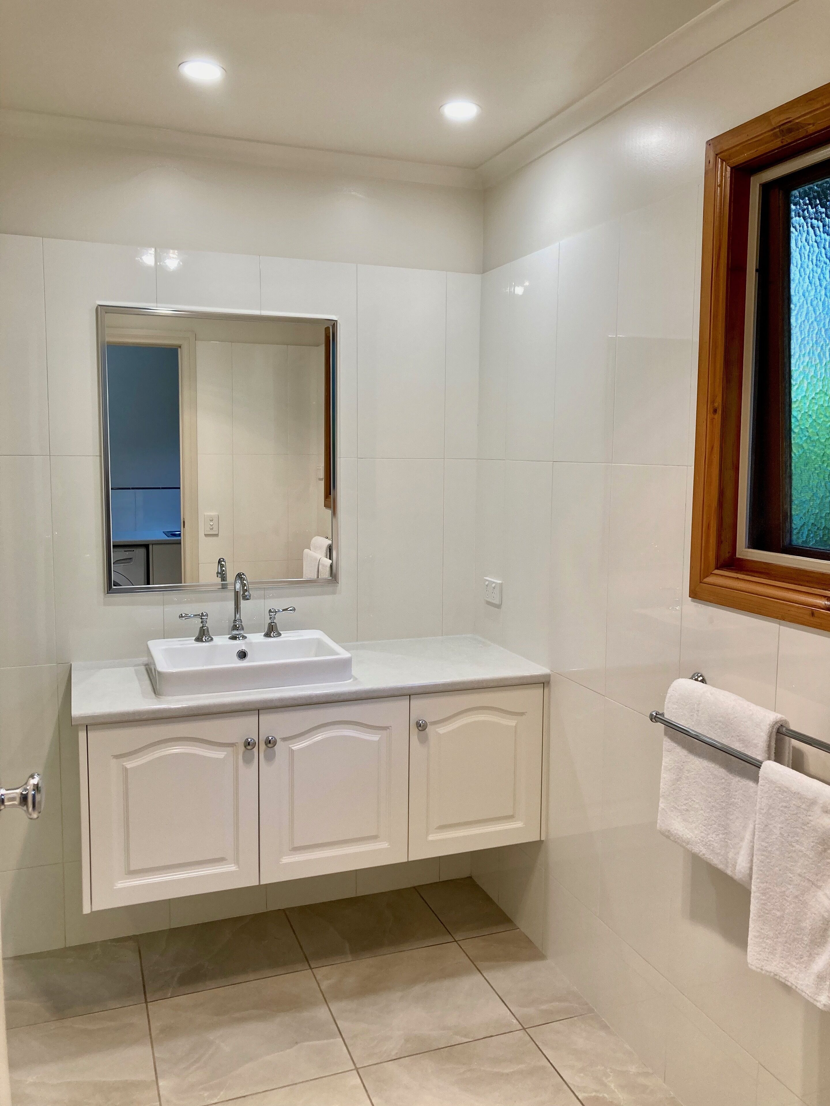 Une salle de bain moderne avec un meuble-lavabo blanc, un grand miroir et une fenêtre avec un cadre en bois.