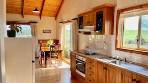 Cozinha com armários de madeira, sala de jantar com mesa e cadeiras, e vista para o exterior através de uma janela.