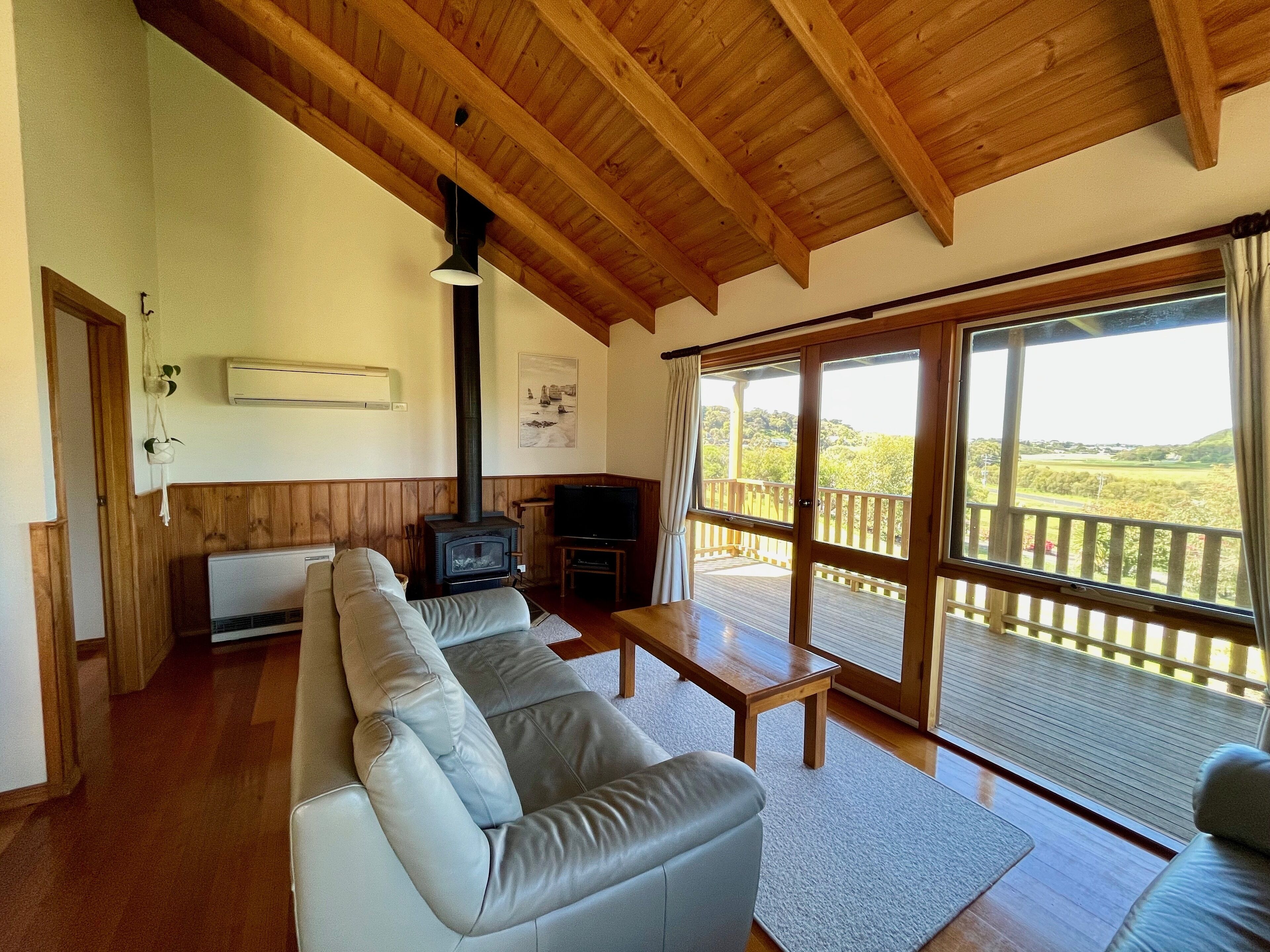 A living room with a sofa, a television, a fireplace, and a balcony with a view of the countryside.