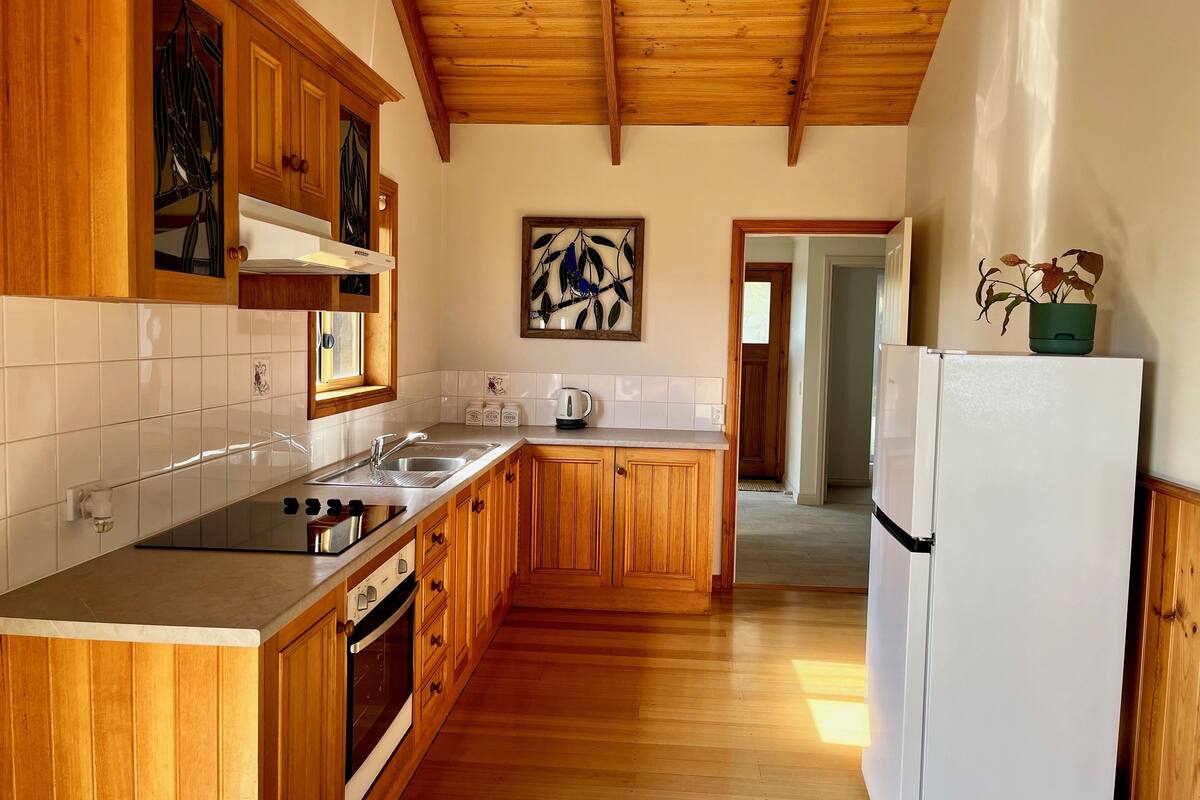 Una cocina con armarios de madera, un lavamanos de acero inoxidable, un refrigerador blanco y un techo de madera.