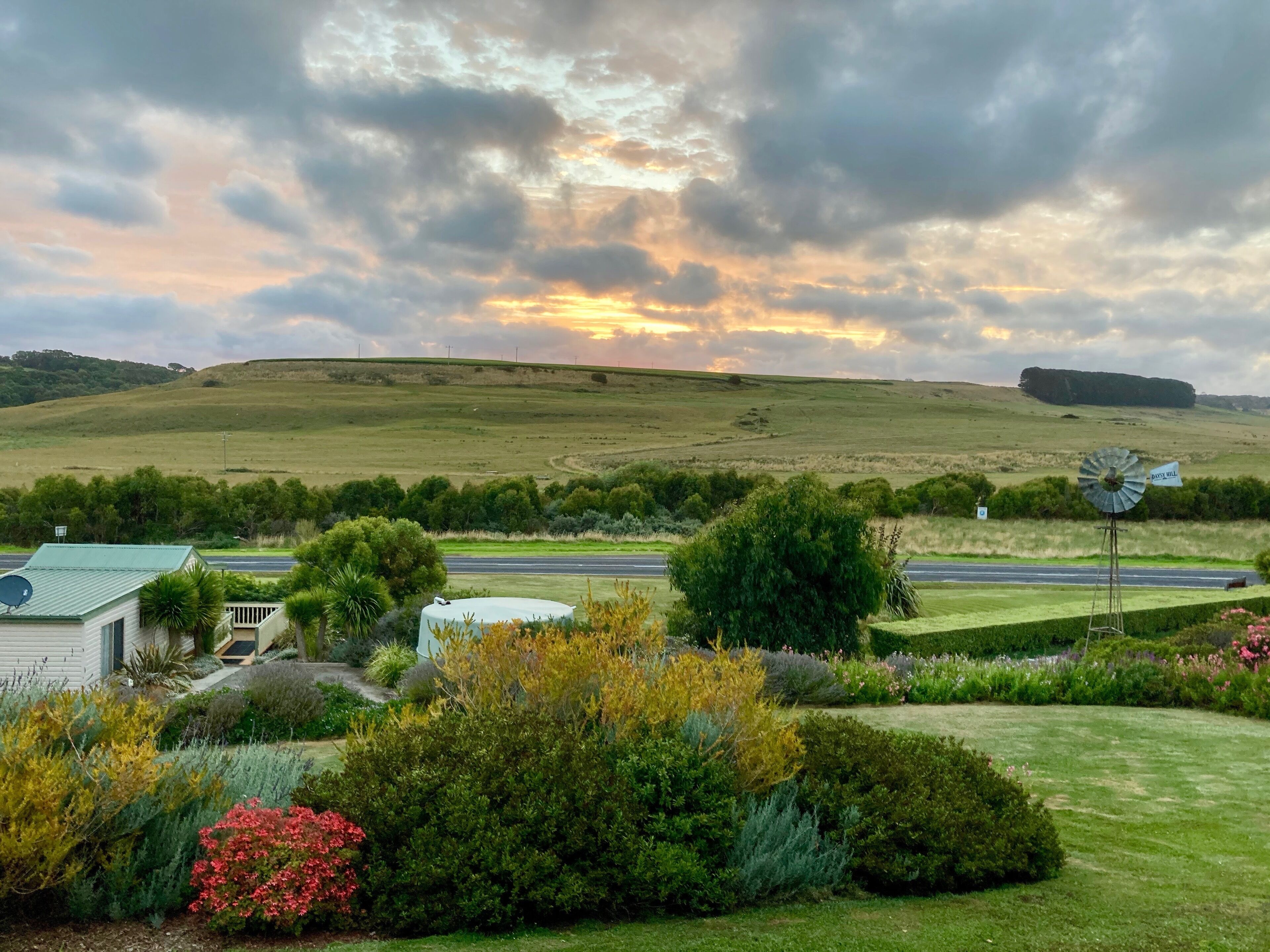 A rural landscape with a windmill, a road, and a house with a satellite dish.