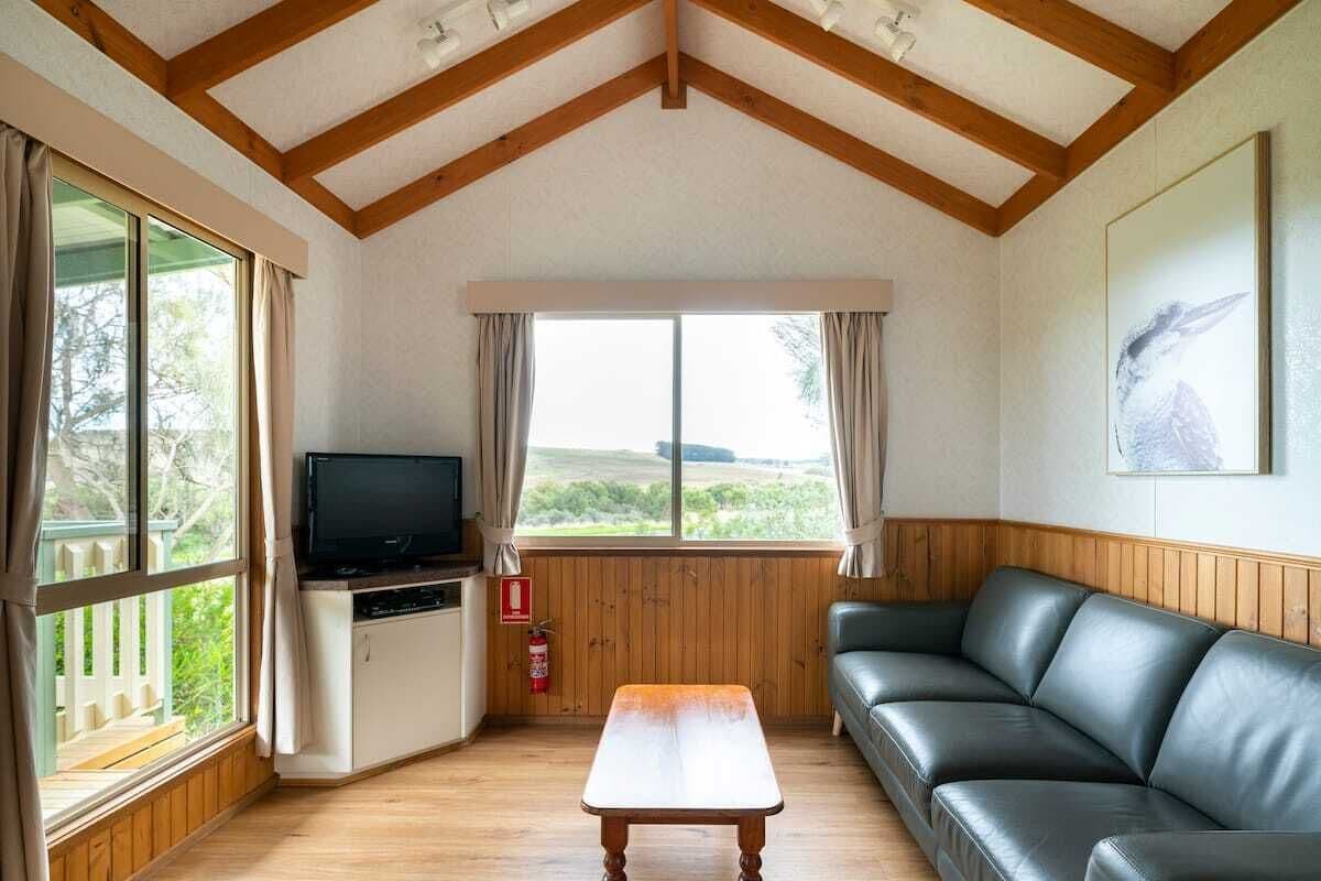 Un salon chaleureux avec un plafond en bois, un canapé en cuir noir, une table basse en bois, un téléviseur et une fenêtre avec des rideaux.