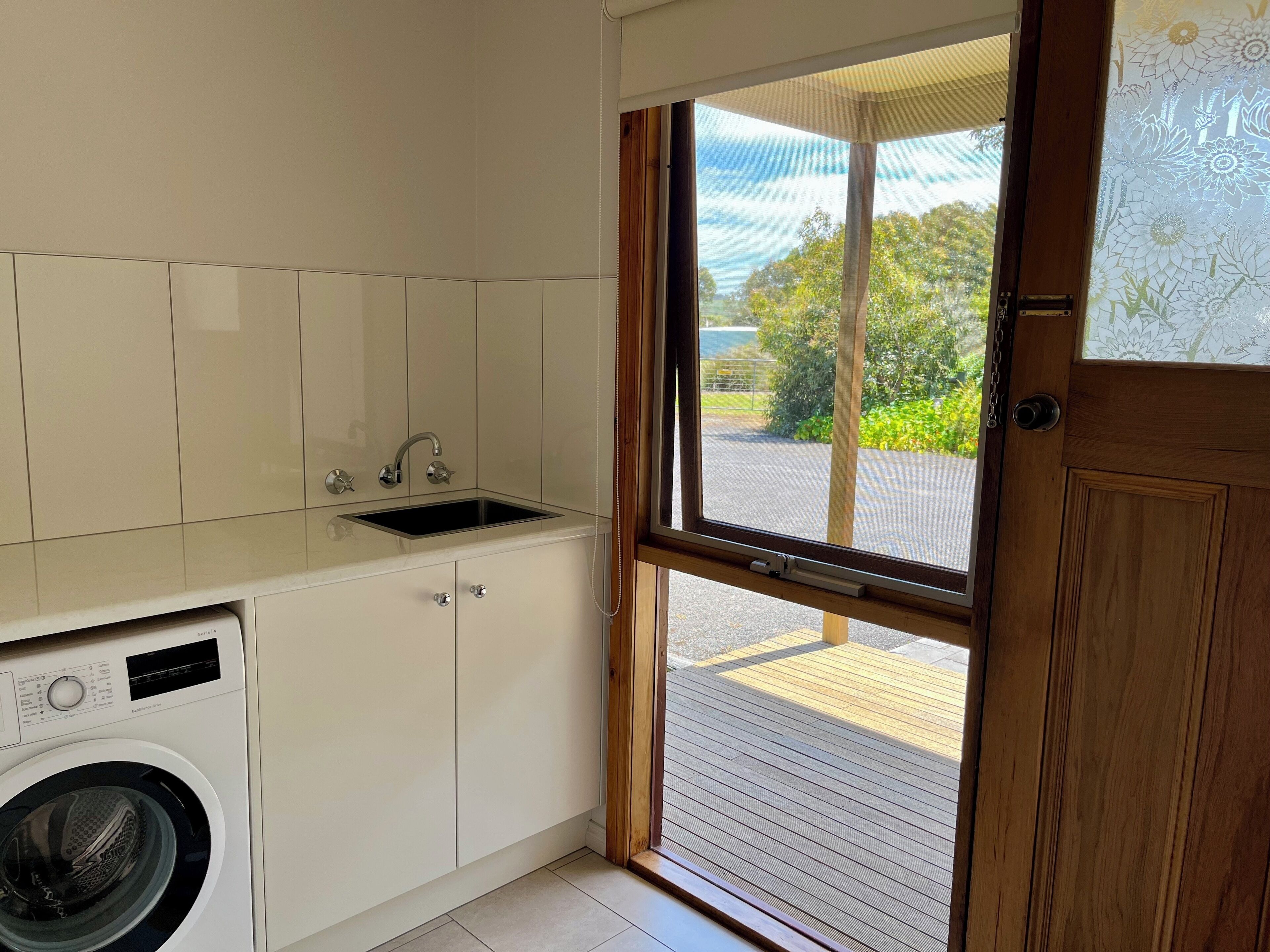 A compact kitchen with a built-in washing machine, a sink, and a window with a view of the outdoors.