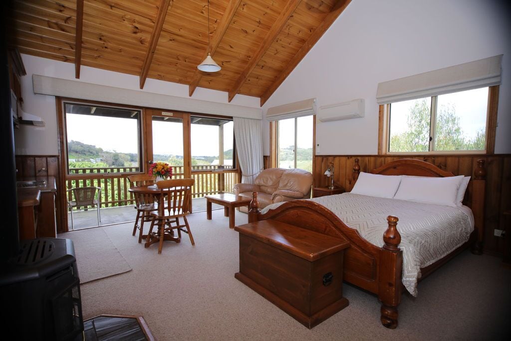 Ein Schlafzimmer mit einem hölzernen Bett, einer Truhe, einem Schreibtisch und einem Stuhl. Ein Balkon bietet Blick ins Freie.