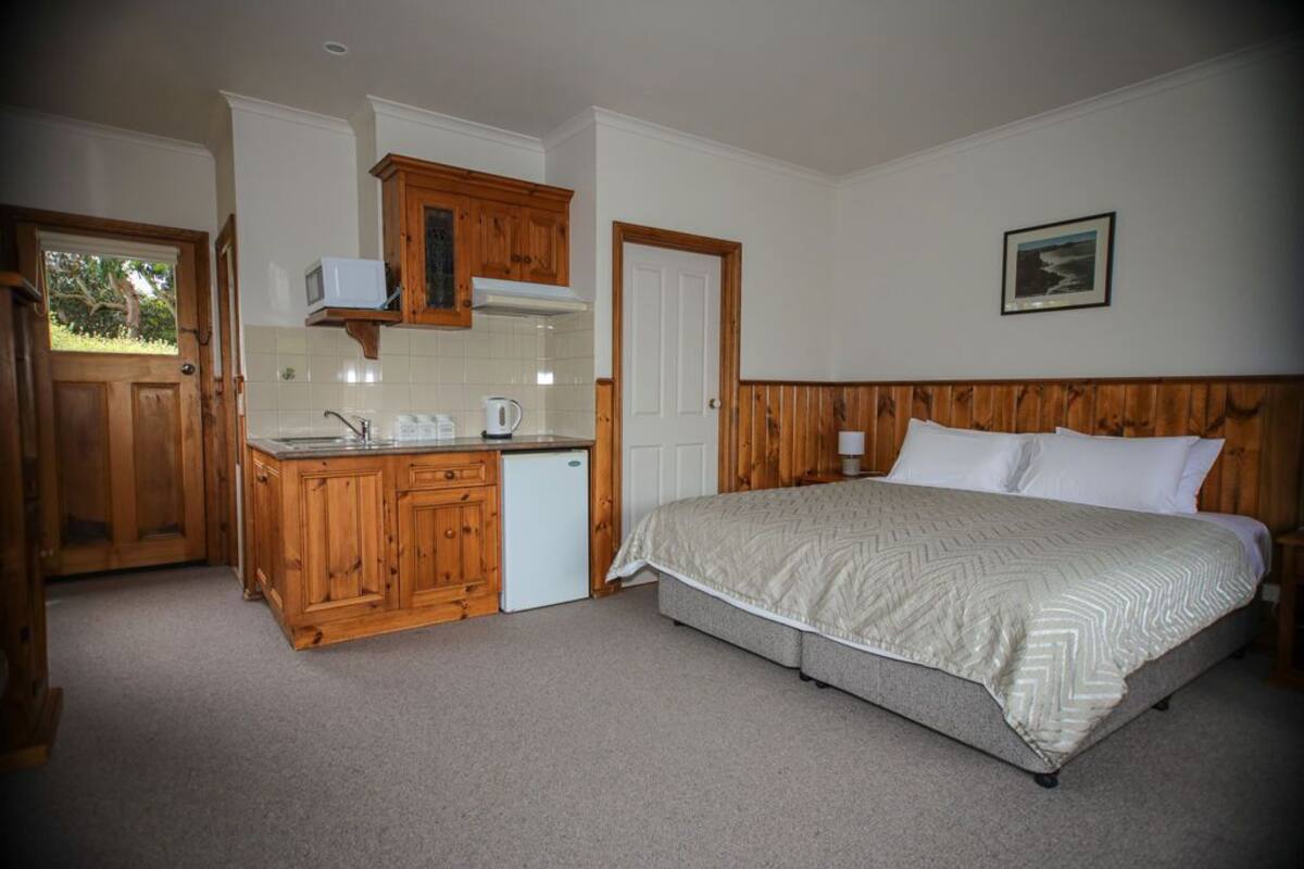 Un dormitorio con una cama grande, cabecera de madera y una pequeña kitchenette con microondas y cafetera.