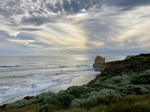 A coastal landscape with a prominent rock formation, waves, and coastal vegetation. - Daysy Hill Country Cottages (Port Campbell)