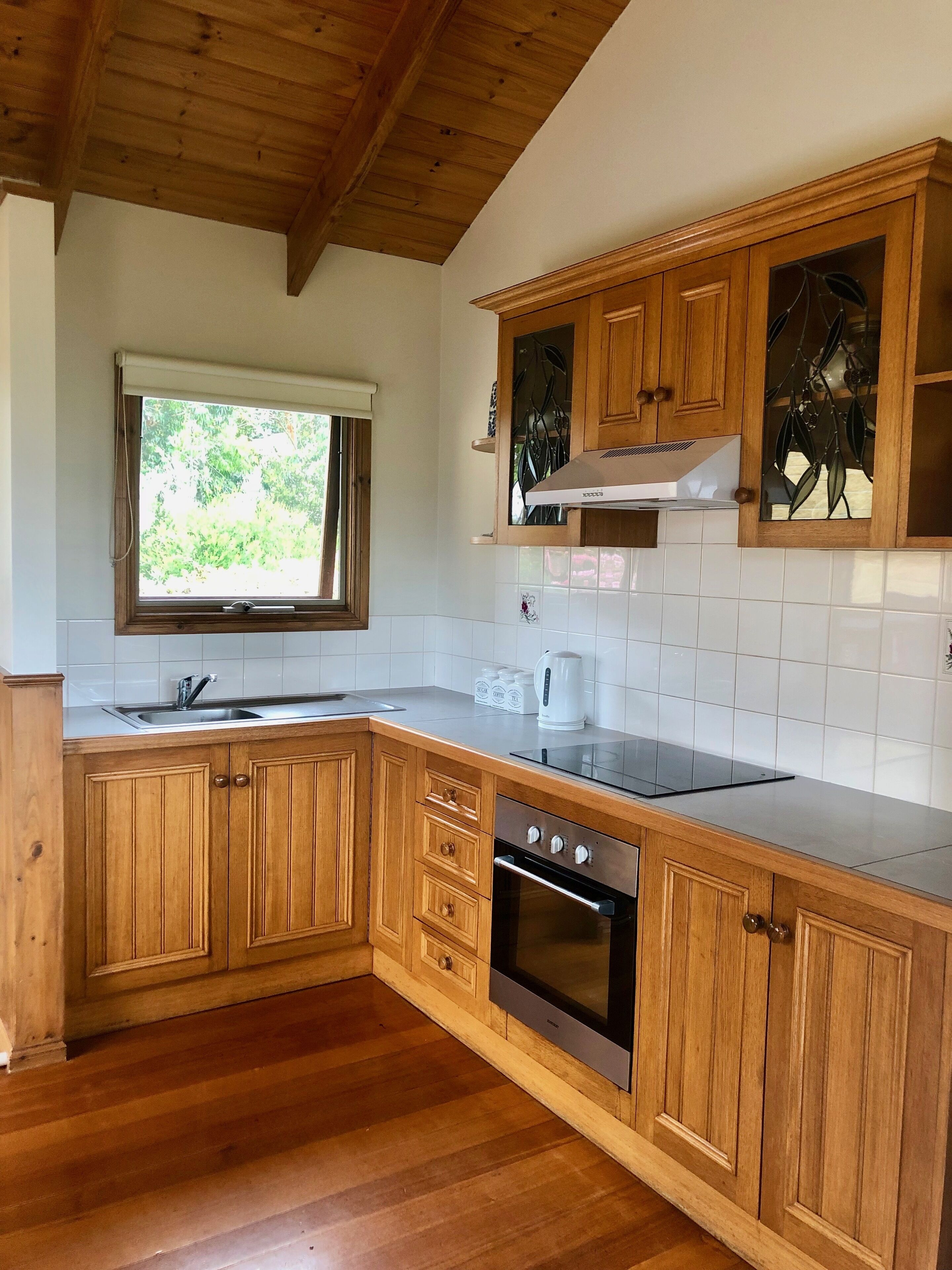 A kitchen with wooden cabinets, a stainless steel sink, a window with a view of greenery, and a built-in oven.
