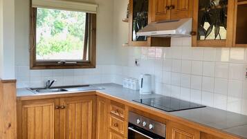A kitchen with wooden cabinets, a stainless steel sink, a window with a view of greenery, and a built-in oven.