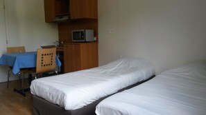 A room with two single beds, a wooden desk, a chair, a microwave, and a table with a blue tablecloth. - Au Relais de Clamart (Clamart)