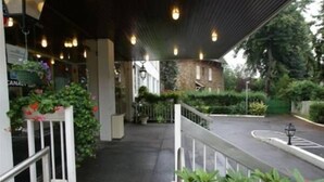 A covered outdoor area with a staircase leading to a building entrance, surrounded by greenery and a paved path. - Au Relais de Clamart (Clamart)