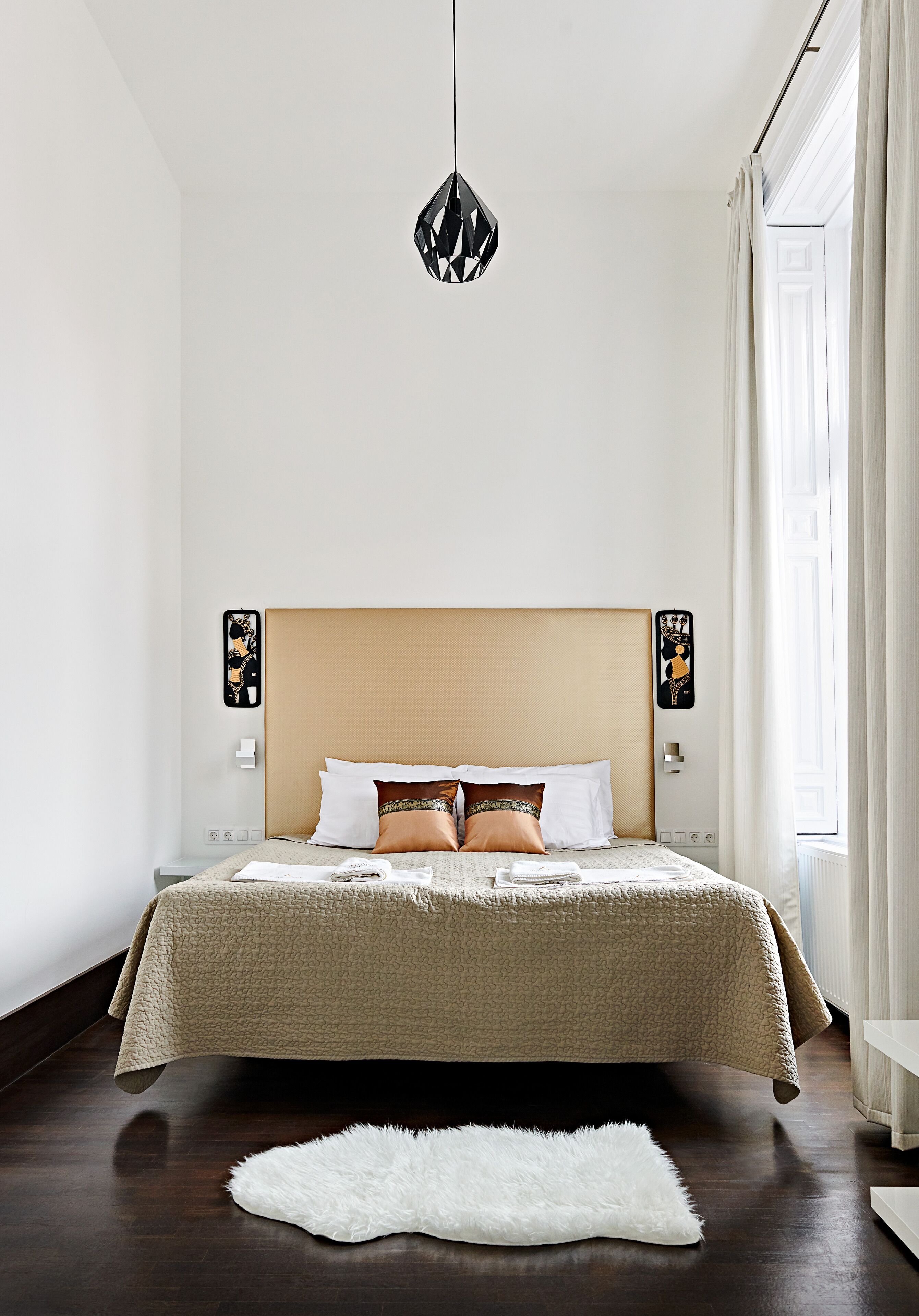 A modern bedroom with a large bed, a hanging light fixture, and a view of the outdoors through a window.