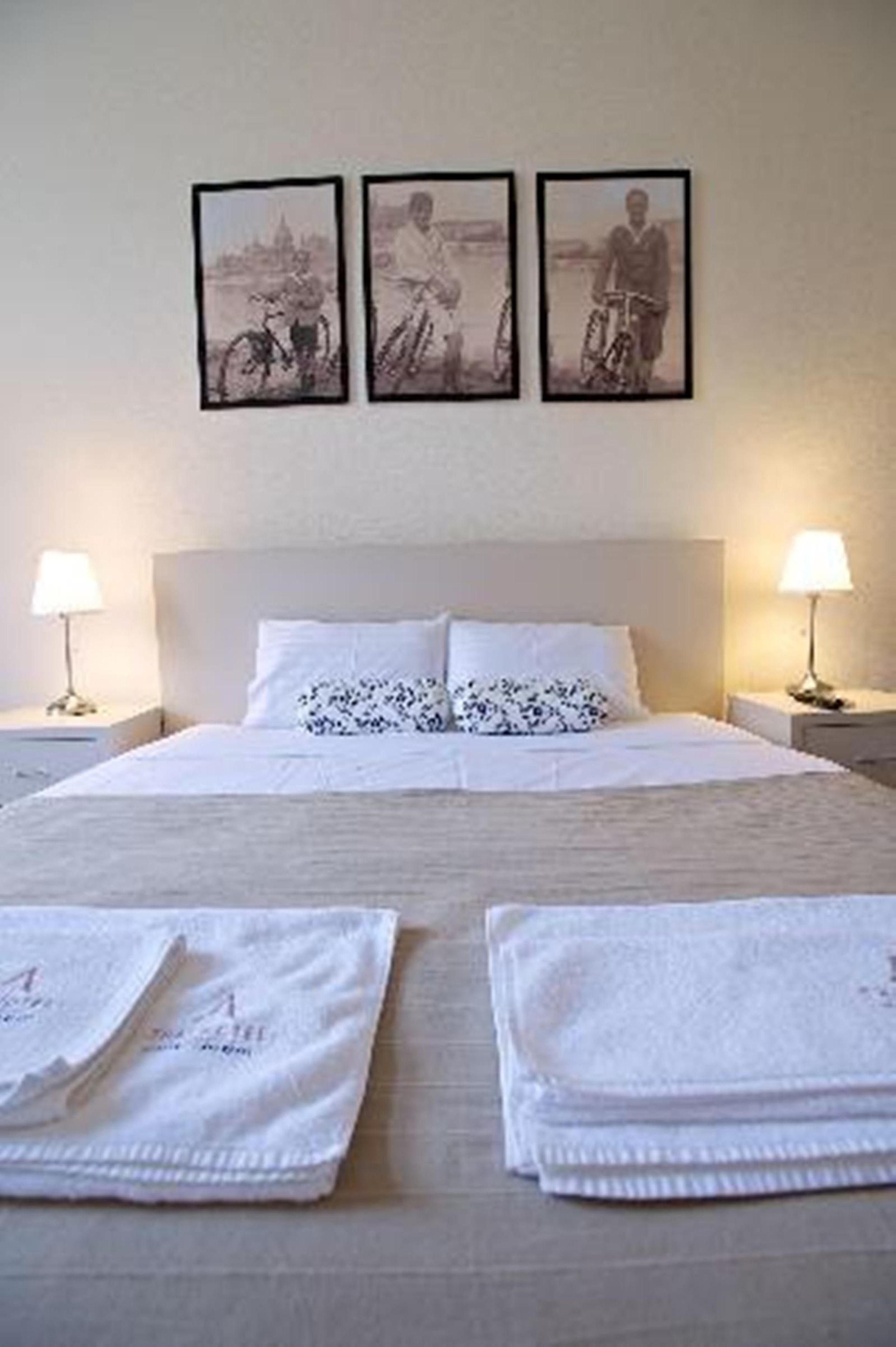 Une chambre d’hôtel avec un lit, deux lampes de chevet, une tête de lit et trois tableaux encadrés accrochés au mur.