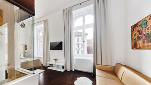 A modern hotel room with a large window, a flat-screen TV, a sofa, and a mirror. - Andrassy Thai Hotel (Budapest)