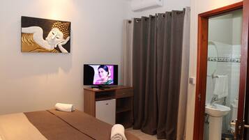 Una habitación de hotel con cama, televisión, un pequeño escritorio, baño con lavamanos e inodoro, y un cuadro en la pared.